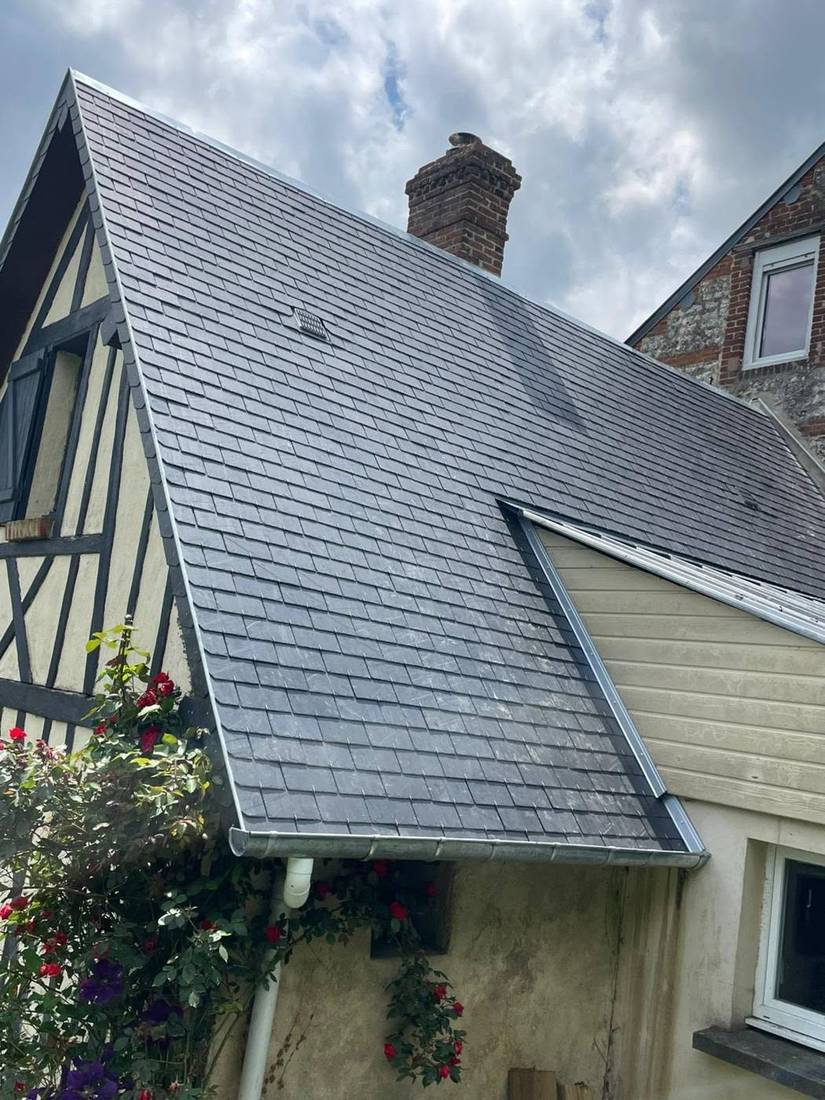 Pan d'ardoise au-dessus d'une maison à colombages fleurie, gouttière en bas de pente