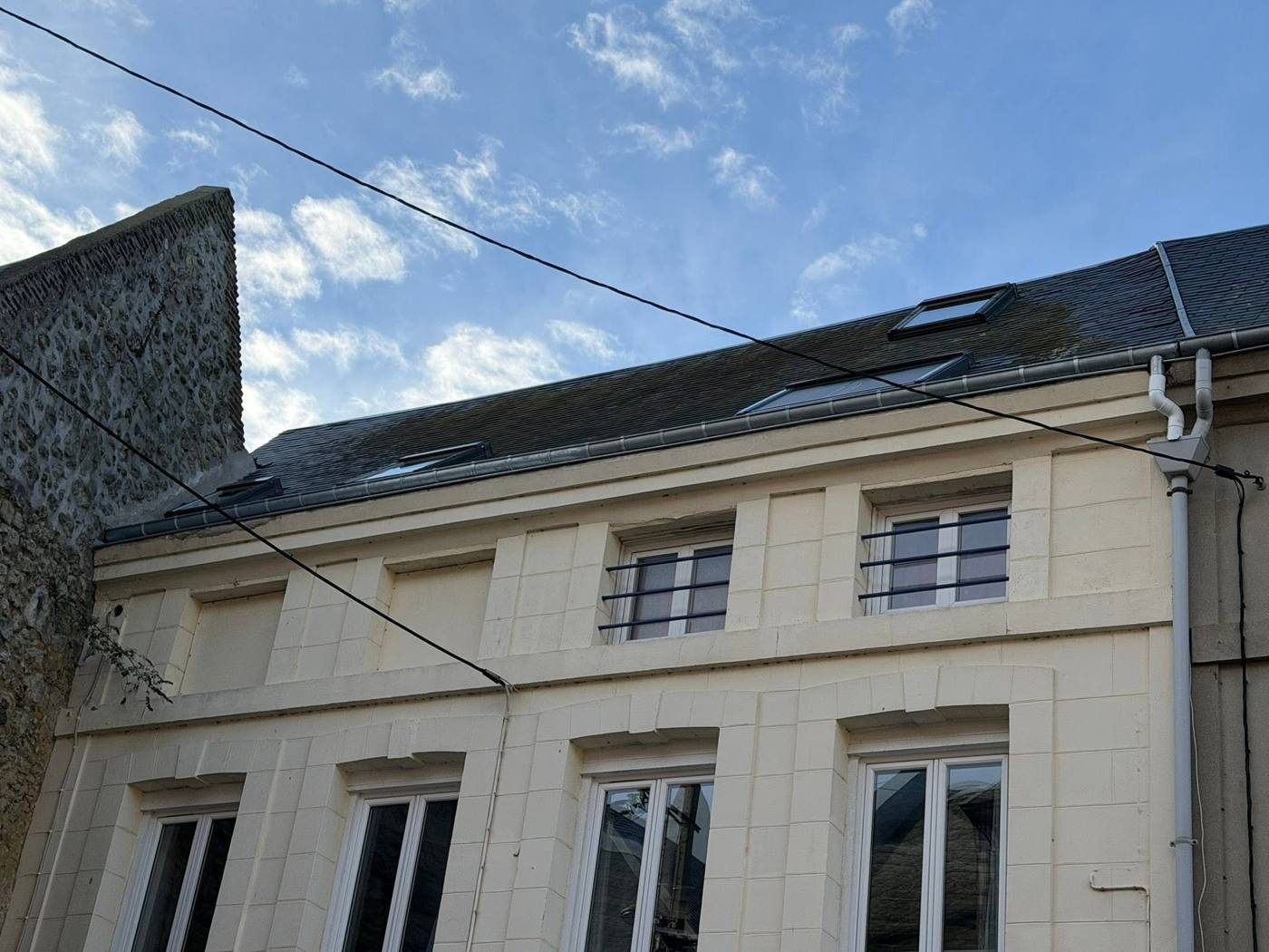 Façade claire à hautes fenêtres, toiture en ardoise avec une fenêtre de toit