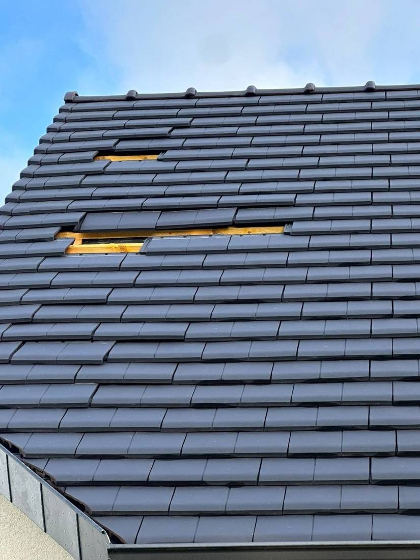 Pan de toiture en tuiles sombres, quelques tuiles déposées pour intervention