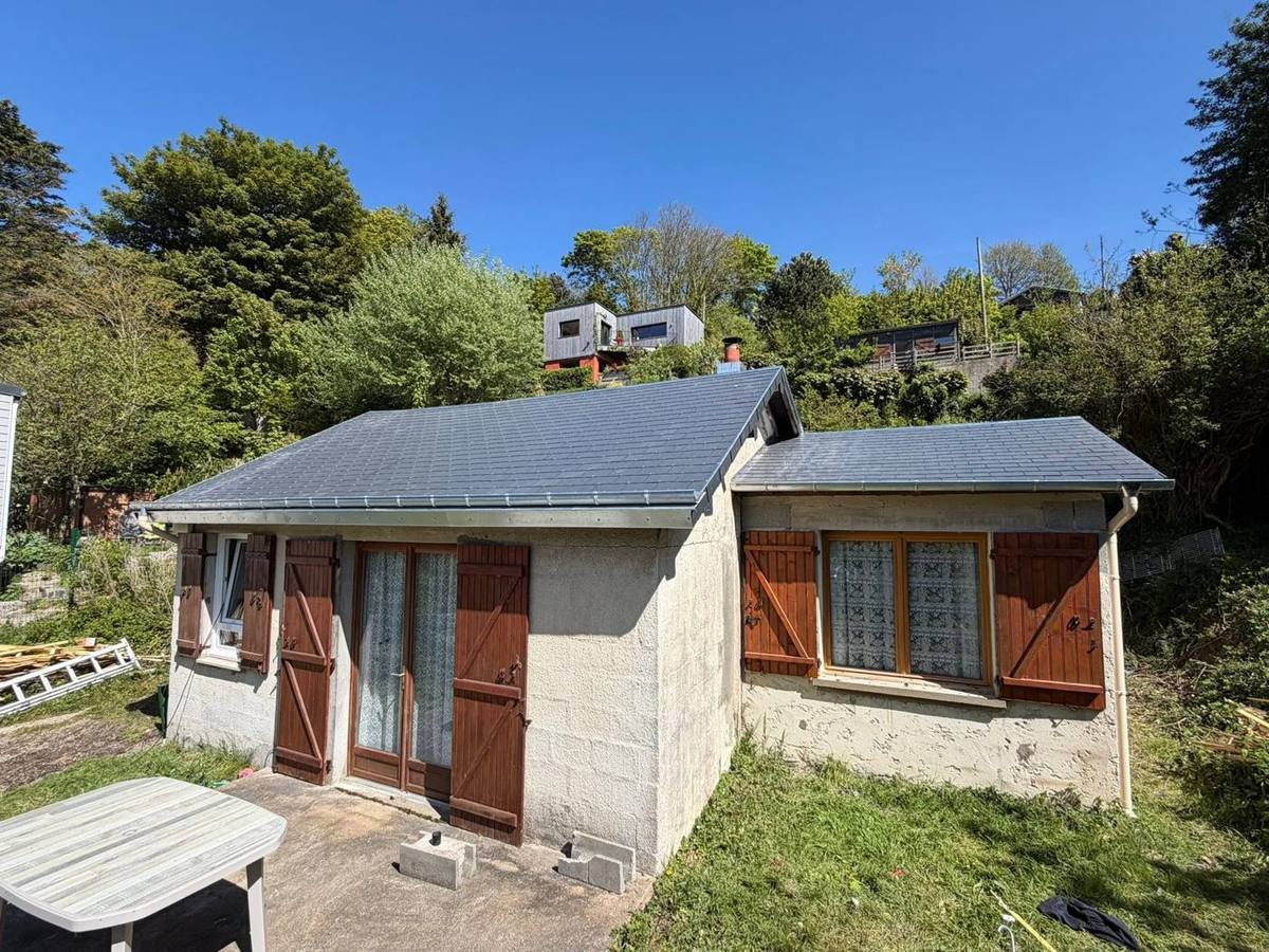 Petite maison à toiture en ardoise au milieu d'un jardin arboré