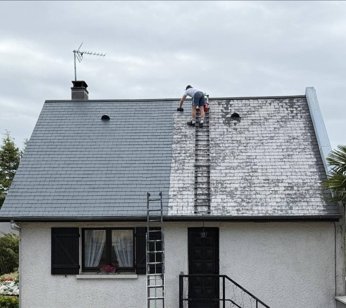 Toiture en ardoise d'une maison blanche pendant le démoussage, couvreur sur une échelle de toit
