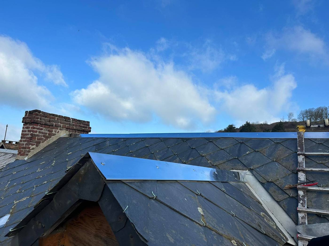 Faîtage et noue en zinc neufs sur une couverture en ardoise, sous un ciel bleu