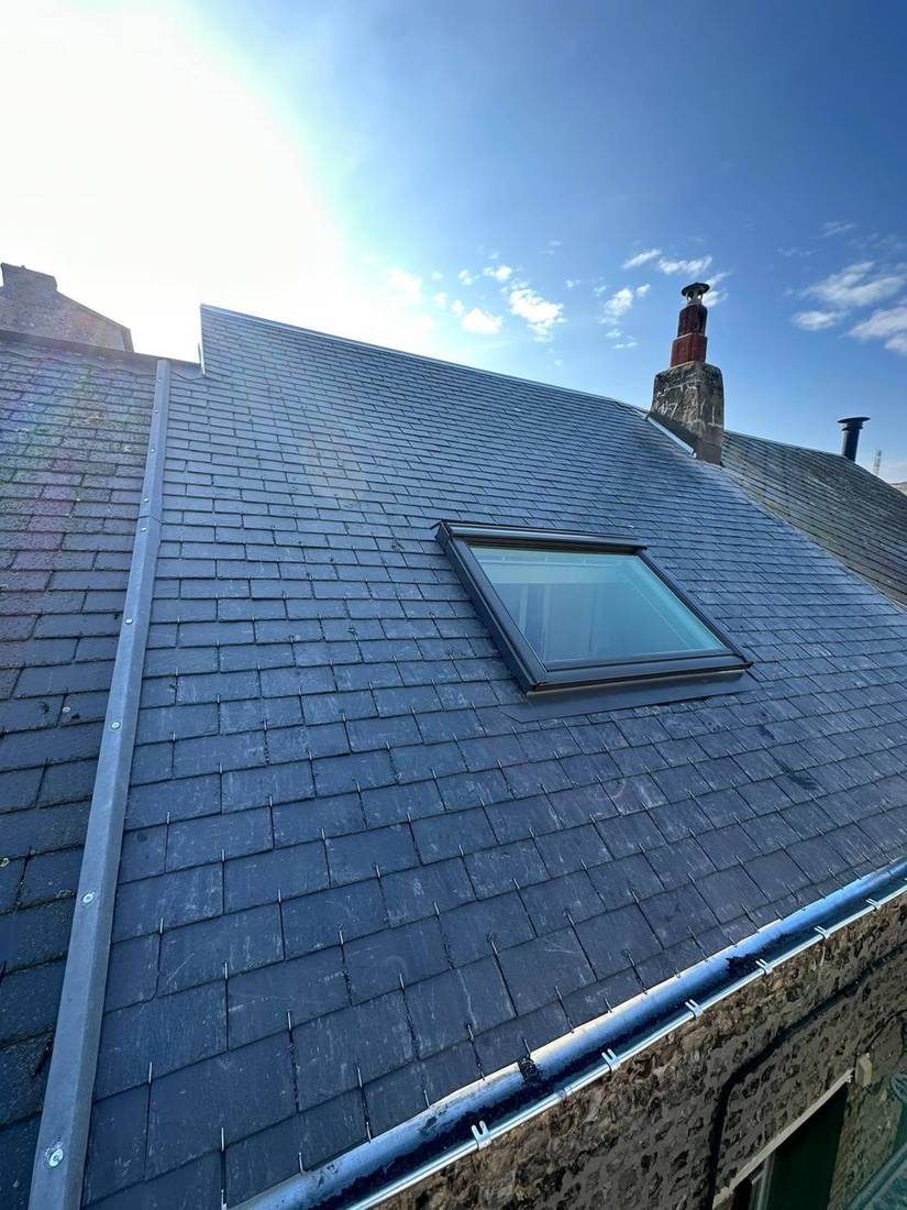 Couverture en ardoise neuve avec une fenêtre de toit, sous un ciel bleu